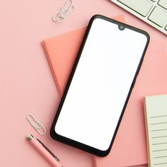 an iphone on top of a pink desk next to a keyboard and notepad with a pen