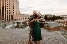 a man and woman standing on top of a wooden deck in front of tall buildings