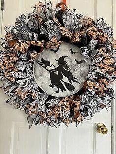 a halloween wreath hanging on the front door with a black and white witch silhouette in it