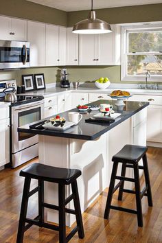 a kitchen with white cabinets, black counter tops and two stools in front of the island