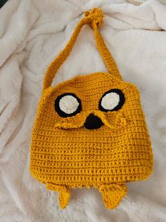 a yellow crocheted bag with eyes and nose on it sitting on a white blanket