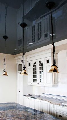 three lights hanging from the ceiling in a kitchen with marble counter tops and white cabinets