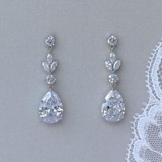 two pairs of diamond earrings are shown on a lace doily, one is white and the other is clear