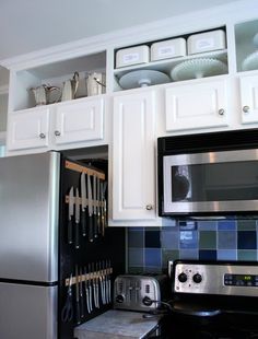 a kitchen with stainless steel appliances and white cupboards on the wall above it is an open shelf that holds utensils