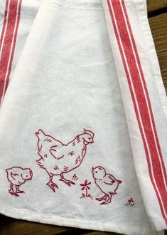 two red and white towels with chickens drawn on them sitting on a wooden table next to each other