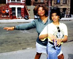 two women are standing on the street with their arms out and one is holding her hand out