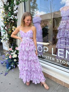 a woman standing in front of a store window wearing a purple tiered dress and sandals