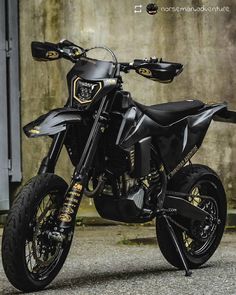 a black and gold motorcycle parked in front of a concrete wall with graffiti on it