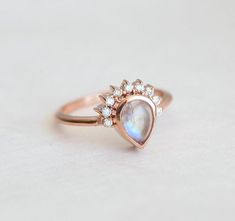 a rose gold ring with a pear shaped rainbow colored stone surrounded by small white diamonds