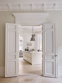 an open door leading to a kitchen and living room with white walls, wood floors and ceiling