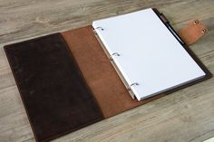 a brown and white notebook sitting on top of a wooden table next to a pen