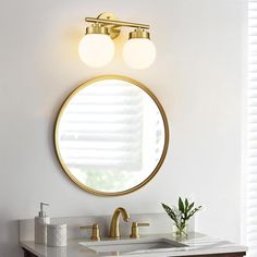 a bathroom vanity with two lights and a round mirror above it, along with a plant on the counter