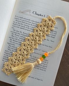 an open book with a tassel on top of it next to a crocheted bookmark