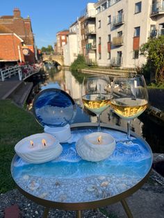 two glasses of wine sitting on top of a table next to a body of water