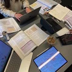 a woman sitting at a table with two laptops and books on it, while looking at the screen