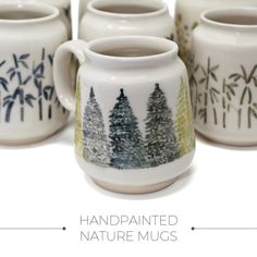 four handpainted mugs with trees painted on the front and sides, all lined up