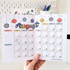 a person holding up a planner with the word august written on it and space themed stickers