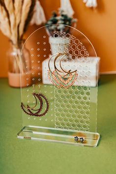 a clear acrylic stand with two earrings on it and a vase in the background