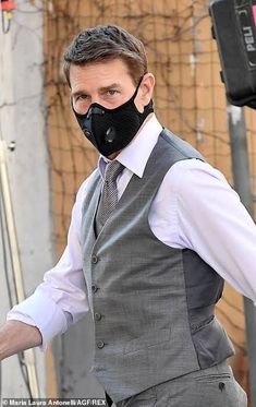 a man wearing a black mask and vest walks down the street with his hands in his pockets