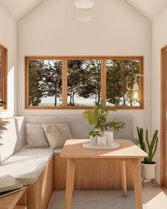 a living room filled with furniture next to two large windows and a wooden table topped with a potted plant