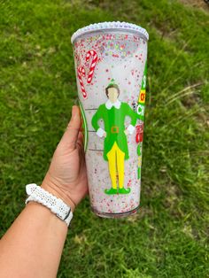 a hand holding up a cup with an image of a elf on it and candy canes