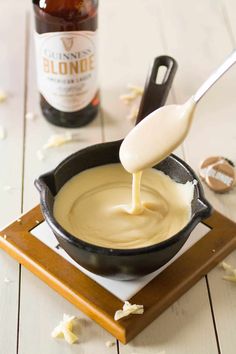 a bottle of beer being poured into a skillet filled with melted cheese and sauce