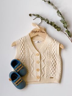 a pair of baby shoes next to a sweater and slippers on a white surface