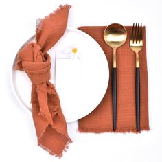 a white plate topped with a fork and knife next to an orange napkin on top of a table