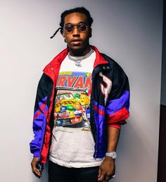 a young man standing in front of a wall wearing sunglasses and a jacket with cars on it