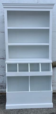 an empty white bookcase sitting on top of a cement floor next to a brick wall