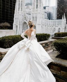 a woman in a white wedding dress standing on the side of a building with her back to the camera