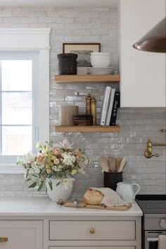 a white kitchen with open shelves and flowers on the counter