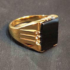 Gold-plated stainless steel. This is a men's style ring with a black flat rectangle simulated onyx stone.  You will look so stylish wearing this affordable and eye-catching ring! The front of the ring is 17mm tall. The black glass stone is 16 x 11.5 mm. Stainless steel jewelry is durable, affordable and TUSK stainless steel is specially treated to equal the brightness and shine of sterling silver and platinum. It is hypoallergenic, extremely resistant to rust, scratching, corrosion and tarnishing.  The gold-plated stainless steel is beautiful and so affordable compared to a solid gold ring. See our other men's statement rings here https://www.etsy.com/shop/BlueMoonTrader?section_id=28033723 and check back as we're going through our whole stash and listing new items weekly. ◄ SHIPPING ►  Sh Black Stone Ring For Men, Stone Rings For Men, Black Stone Ring, Mens Gold Rings, Golden Ring, Solid Gold Rings, Mens Gold, Onyx Stone, Black Stone