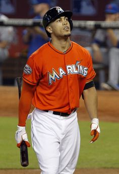 a baseball player is walking on the field with his bat in one hand and wearing an orange jersey