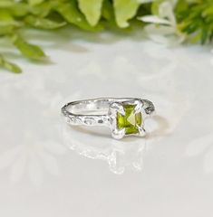 Show your love with this exquisite Peridot ring. Handcrafted in wax and cast in Solid Silver, this stunning green crystal ring features an organic textured band, ensuring its uniqueness. Adorned with a mesmerizing princess-cut Peridot, also the August birthstone, it embodies more than an engagement ring - it symbolizes timeless love and individualityT H E ∙ S M A L L ∙ D E T A I L S• Princess-cut Peridot (5 x 5mm)• Sterling Silver textured bandM A T E R I A L ∙ O P T I O N S• Sterling Silver• So Silver Peridot Ring, Peridot Ring Silver, Green Crystal Ring, Timeless Love, August Birthstone, Peridot Ring, Green Crystal, Crystal Ring, August Birth Stone