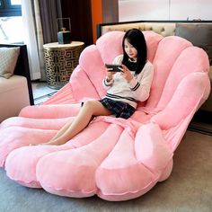 a woman sitting on a giant pink bean bag chair holding a cell phone in her hand