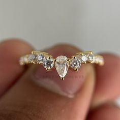 a hand holding a gold ring with three pear shaped diamonds on it's side