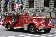 an old fire truck driving down the street with flags on it's back end