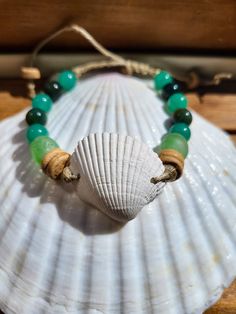 This handmade, natural beaded hemp bracelet features a clam shell framed by coconut shell beads, green recycled glass beads made in Africa, and fancy jasper and aventurine gemstones. The gemstone beads are 8mm size. The shell measures approximately 1.5 inches wide and 1.5 inches tall. The bracelet uses a sliding macrame knot to allow easy on/off and adjustability. I pull all of the seashells from the sand myself. Every purchase removes one pound of trash from a beach! Artisan Green Beaded Bracelets For Beach, Bohemian Adjustable Bracelets With Recycled Glass, Adjustable Bohemian Bracelets With Recycled Glass, Adjustable Bohemian Bracelet With Recycled Glass, Adjustable Bohemian Bracelets Made Of Recycled Glass, Earthy Green Beaded Bracelets With Gemstone Beads, Green Earthy Beaded Bracelet With Gemstone Beads, Earthy Hand Wrapped Bracelets For Beach, Earthy Natural Stone Beaded Bracelets For Beach