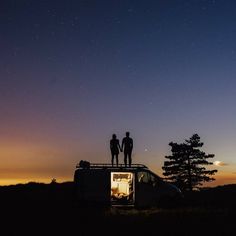 two people standing on the roof of a van at night with stars in the sky