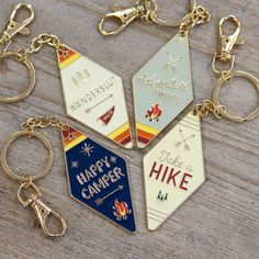 four different key chains with happy camper and hike tags on them, sitting on a wooden surface