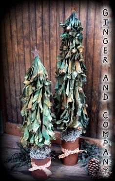 two christmas trees made out of fake leaves on top of potted plants and pine cones