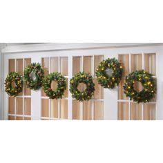 christmas wreaths are hung on the side of a door with lights around them and in front of windows