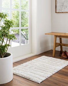 a white rug on the floor in front of a window with a potted plant next to it