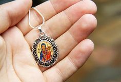 a hand holding a pendant with an image of the virgin mary