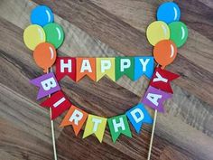 a happy birthday cake with balloons and streamers on it's head, sitting on a wooden table