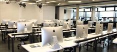 an empty computer lab with white desks and computers on the tables in front of large windows