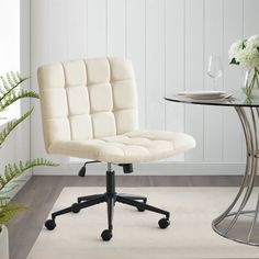 a white office chair sitting next to a table with flowers on it and a glass vase