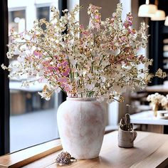 a vase filled with white and pink flowers on top of a wooden table next to a window