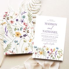 the wedding stationery is laid out on top of white fabric and has flowers painted on it